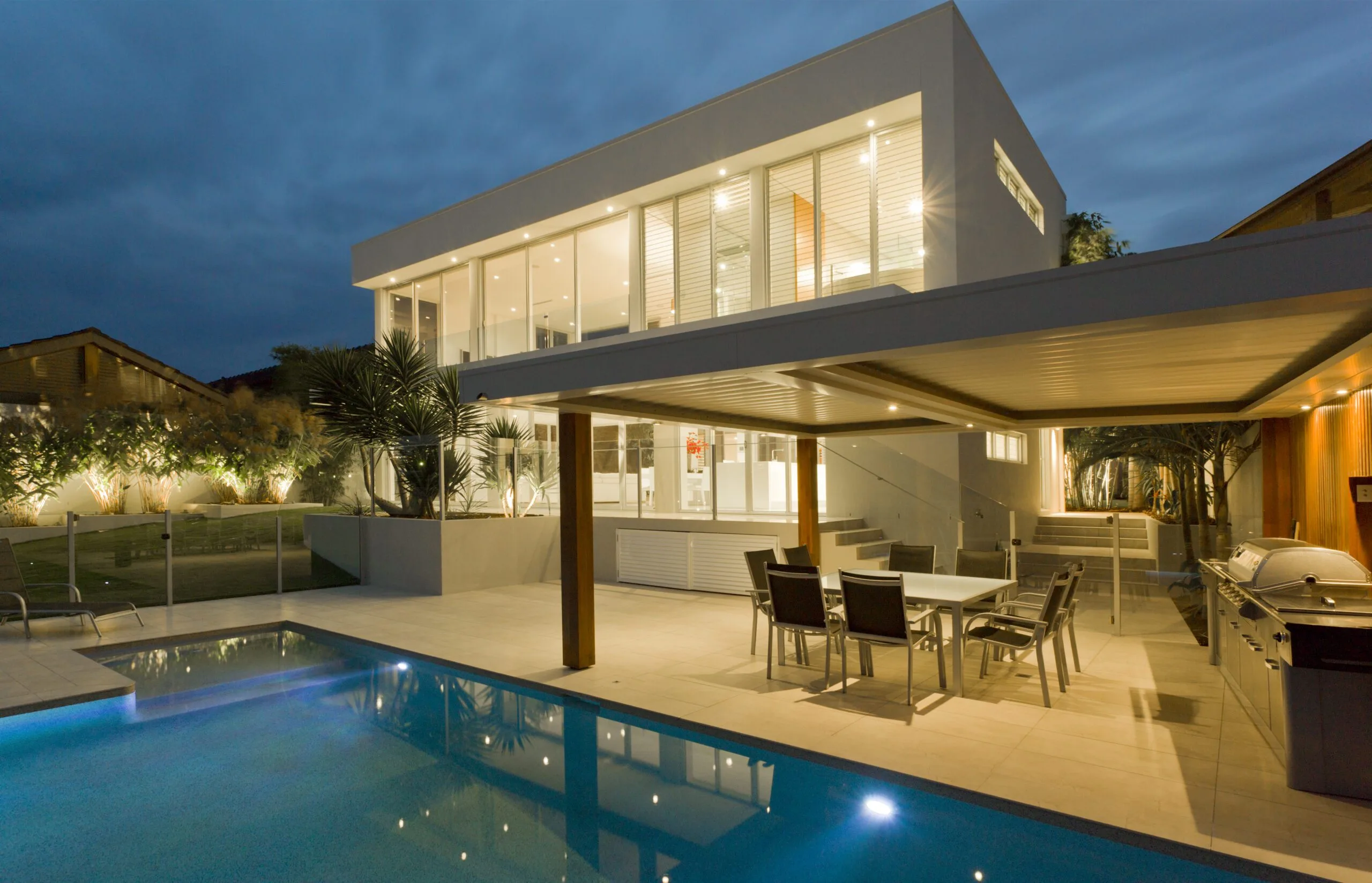 Modern,House,At,Dusk,With,Swimming,Pool,And,Barbecue,In Modern house at dusk with swimming pool and barbecue in backyard